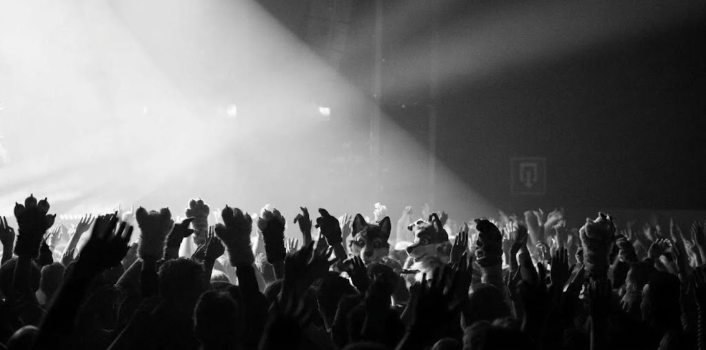Crowd of furries with raised paws in front of a lit stage